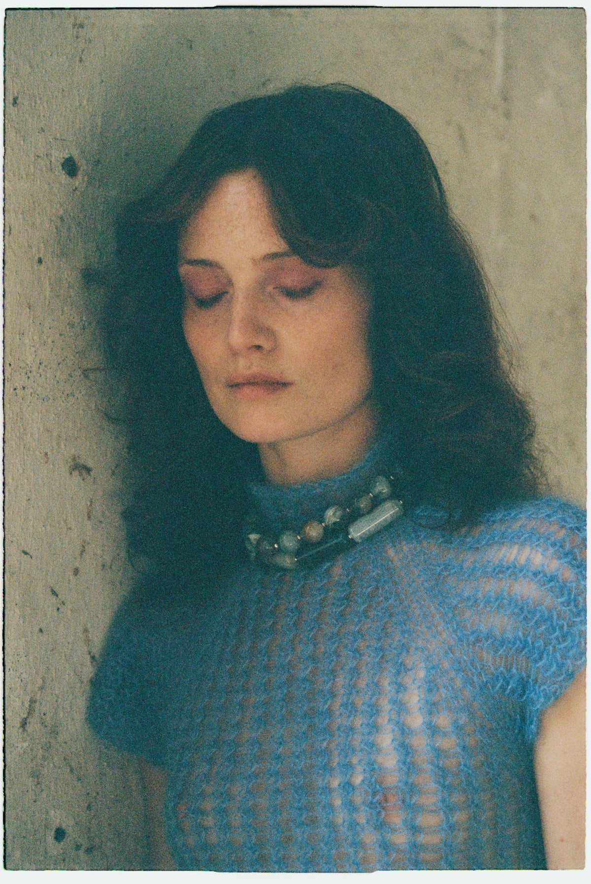 Model wearing a blue open-knit top and a beaded stone necklace